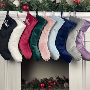 May include: Set of 10 velvet Christmas stockings with personalised names, including "Dad" and "Mom". The stockings are in various colours, including black, white, red, green, pink, blue, grey, and purple.