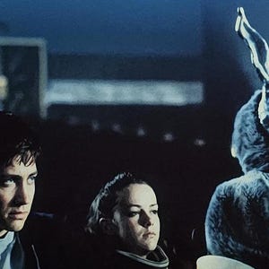 Puede incluir: Una escena de una pel&iacute;cula con tres personas. Una persona lleva un amenazante disfraz de conejo con una cara esquel&eacute;tica. Las otras dos personas miran fuera de la pantalla con expresiones serias. El fondo es oscuro.