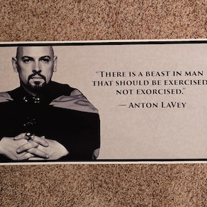 May include: Black and white poster featuring a portrait of a man with a quote by Anton LaVey: "THERE IS A BEAST IN MAN THAT SHOULD BE EXERCISED, NOT EXORCISED." The poster has a black border and is displayed on a neutral background.
