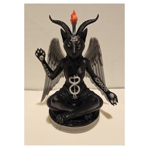 May include: A black figurine of a seated horned creature with grey wings, a white flame on its head, and a white pentagram on its forehead. The word SLEEP is printed on the right arm and CHAOS on the left arm, with a white caduceus symbol on the torso.