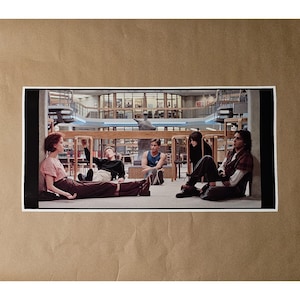 May include: A print featuring a scene from the movie "The Breakfast Club." The image shows five young people sitting and leaning in a library setting. The background includes bookshelves and architectural details.