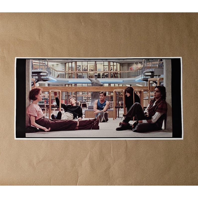 May include: A print featuring a scene from the movie "The Breakfast Club." The image shows five young people sitting and leaning in a library setting. The background includes bookshelves and architectural details.