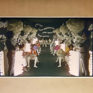 May include: A scene from a fashion show with mannequins and figures in a dark room. The mannequins have white wigs and are arranged on either side of a runway. Figures in colorful outfits are seated on the runway.