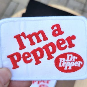 May include: White embroidered patch with red text that reads "I'm a Pepper" and the Dr Pepper logo.