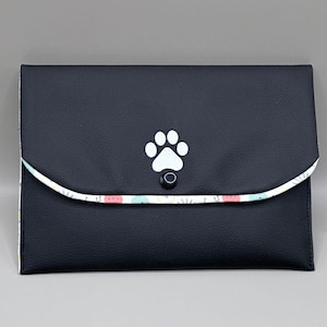 Peut inclure: Une pochette noire avec une empreinte de patte blanche et une fermeture à bouton décorative. Le rabat est doublé d'un tissu à motifs avec des éléments roses, bleus et blancs. Cet accessoire est idéal pour transporter l'essentiel.