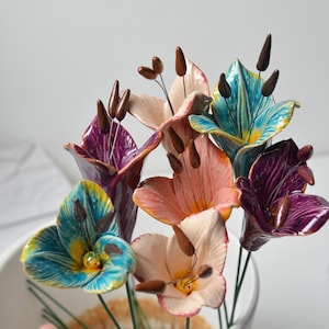 Puede incluir: Un ramo de flores de cerámica en varios colores, incluyendo rosa, morado, azul y amarillo. Las flores están dispuestas en un jarrón y tienen un aspecto realista.