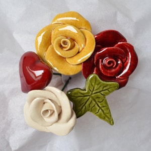 May include: A set of five ceramic flower decorations, including three roses in yellow, red, and white, a heart, and a green leaf.