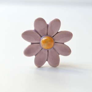 K&ouml;nnte beinhalten: Ein Keramik-Blumenknauf mit einem lila G&auml;nsebl&uuml;mchen-Design und einer gelben Mitte.