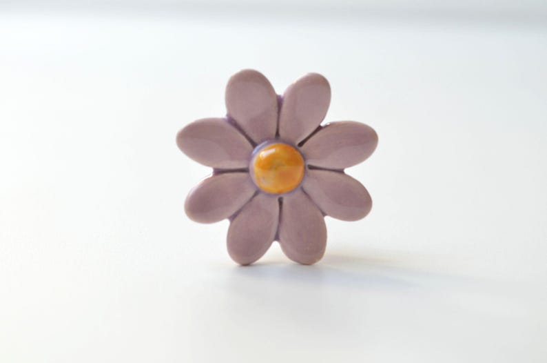 K&ouml;nnte beinhalten: Ein Keramik-Blumenknauf mit einem lila G&auml;nsebl&uuml;mchen-Design und einer gelben Mitte.