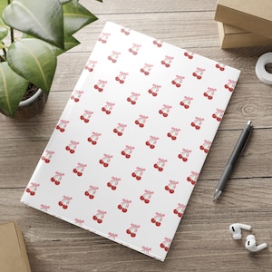 May include: White notebook cover with a repeating pattern of pink cherries with pink bows.