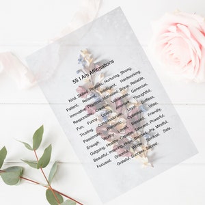 Peut inclure: Une carte blanche avec le texte "55 I Am Affirmations" et une liste de 55 affirmations positives imprimées en noir. La carte est décorée de fleurs séchées.