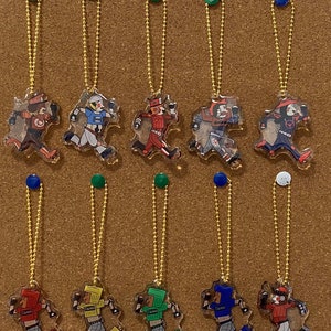 May include: Ten colorful keychains featuring cartoon characters wearing different colored jerseys and helmets. Each keychain has a gold chain and a clear plastic background.