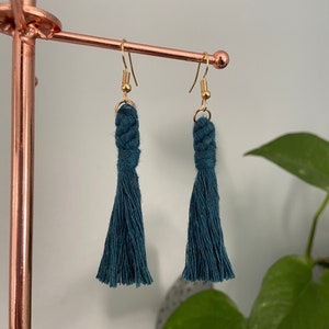 May include: Teal blue tassel earrings with gold hooks. The tassels are made of a soft, woven material and have a knotted top.