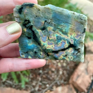 Può includere: Un pezzo di labradorite con colori iridescenti blu, verdi e dorati. La pietra ha una texture ruvida e naturale ed è una scelta popolare per gioielli e guarigione con cristalli.