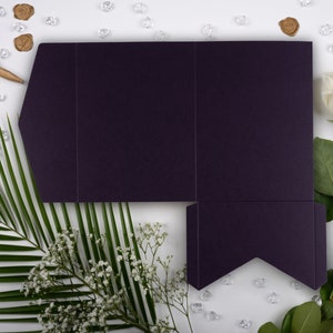 May include: A deep purple folded card with a decorative edge, surrounded by white flowers, green leaves, and clear crystals.