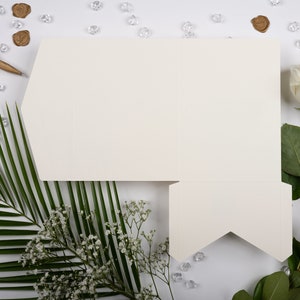 Puede incluir: Una tarjeta blanca con un diseño plegado, rodeada de hojas de palmera verdes, flores blancas y una rosa blanca con hojas verdes. También hay pequeños cristales transparentes y sellos de cera marrón esparcidos alrededor de la tarjeta.