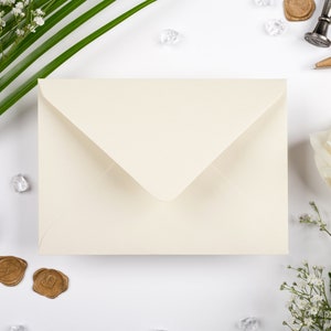May include: A white envelope with a folded flap, surrounded by white flowers, green leaves, and gold wax seals on a white background.