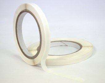 May include: Two rolls of white double-sided tape. The tape is on a white background.