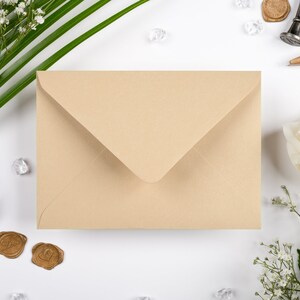 May include: A light brown envelope with a white background. The envelope is surrounded by white flowers, green leaves, and small clear glass beads.
