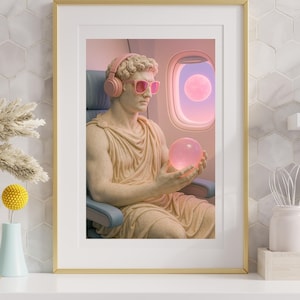 May include: Framed art print featuring a classical statue wearing pink sunglasses and headphones, holding a glowing orb. The statue is seated on an airplane, with a pink moon visible through the window. The artwork is in a gold frame.