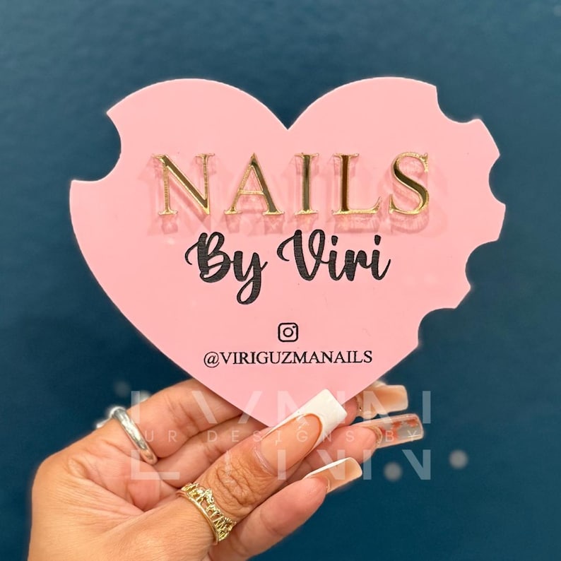 May include: Pink heart-shaped sign with the text "NAILS By Viri" and the Instagram handle "@VIRIGUZMANAILS" in black text.