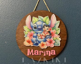 May include: A wooden round sign with a brown background featuring Stitch and Lilo from the Disney movie Lilo & Stitch. Stitch is blue and Lilo is wearing a pink dress. The sign has pink flowers and green leaves around the characters. The name "Marina" is written in pink letters at the bottom of the sign.