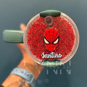 May include: A green and clear tumbler with a red glitter base. The tumbler has a green lid with a red and blue Spiderman character and the name "Santino" written in blue.