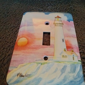 May include: A white lighthouse with a red roof stands on a rocky cliff overlooking a blue ocean. The sky is a watercolor of pink, orange, and yellow. The image is printed on a light switch cover.
