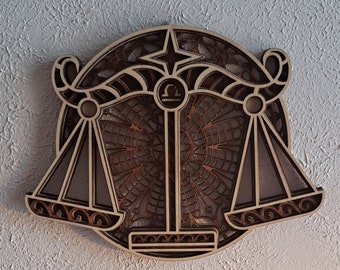 May include: A wooden wall decor featuring a stylized Libra zodiac sign with intricate details. The scales are balanced and the design is framed by a circular mandala pattern.