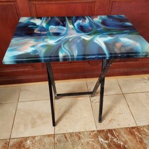 May include: A small, blue, green, and white epoxy resin table top with a black metal folding frame.