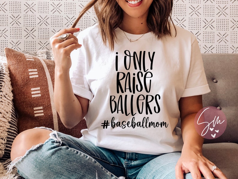 May include: White t-shirt with black text that reads "I only raise ballers #baseballmom".