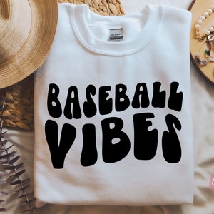 May include: White sweatshirt with the text "BASEBALL VIBES" in black, retro-style lettering.