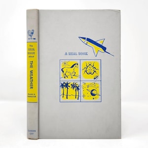 May include: A light gray hardcover book titled The Real Book about THE WEATHER by Frank H. Forrester. The cover features a blue and yellow rocket, the text A REAL BOOK, and a square grid with illustrations of a horse, ladybug, palms, and space.