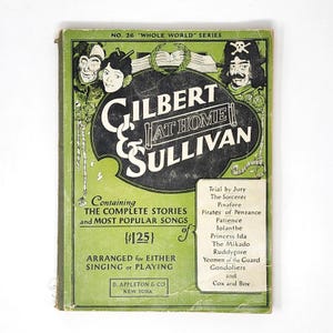 May include: A vintage green music book titled Gilbert & Sullivan At Home from the Whole World Series, No. 26. The cover features black illustrations of characters, a list of operas including The Mikado and Pirates of Penzance, and text.
