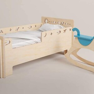 May include: A wooden toddler bed with a white sheet and a blue rocking horse. The bed has a decorative cutout design of stars, moons, and a sun.