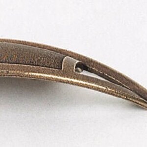 May include: A curved, bronze-colored cabinet pull with a textured finish. The pull has a simple, elegant design with a slight arch.