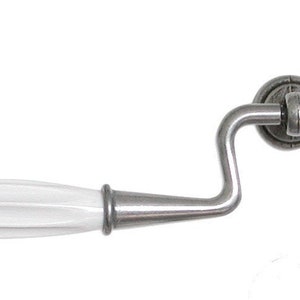 May include: A white ceramic cabinet pull with a silver finish. The pull has a curved design and a fluted handle.