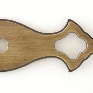 May include: A brass-colored decorative plate with a central hole and two ornate cutouts on either side. The plate has a slightly curved shape and a brushed finish.