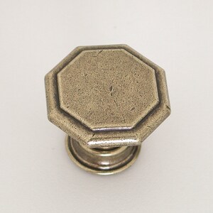May include: An antique brass octagonal cabinet knob with a raised edge and a smooth, slightly textured surface.