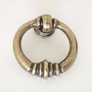 May include: A circular, antique brass ring pull cabinet handle with a decorative, ribbed design.