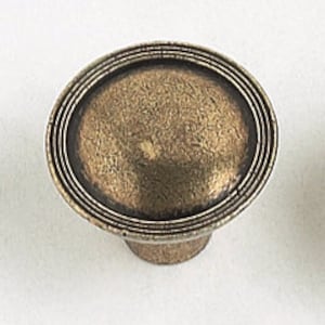 May include: A round, antique brass cabinet knob with a raised, domed center and three concentric rings around the edge.