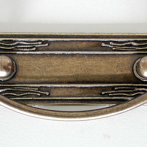 May include: A rectangular, antique brass drawer pull with a decorative, etched design and a curved handle.