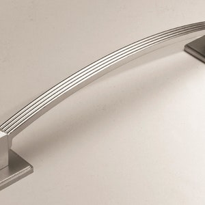 May include: A silver-toned, arched cabinet pull with a square base and a decorative, grooved design.