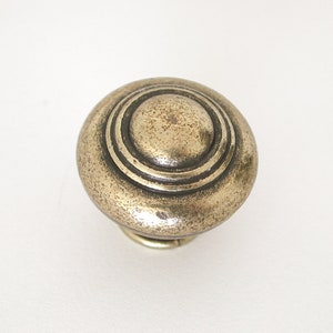 May include: A round, silver-toned cabinet knob with a raised, textured center and three concentric rings around the edge.