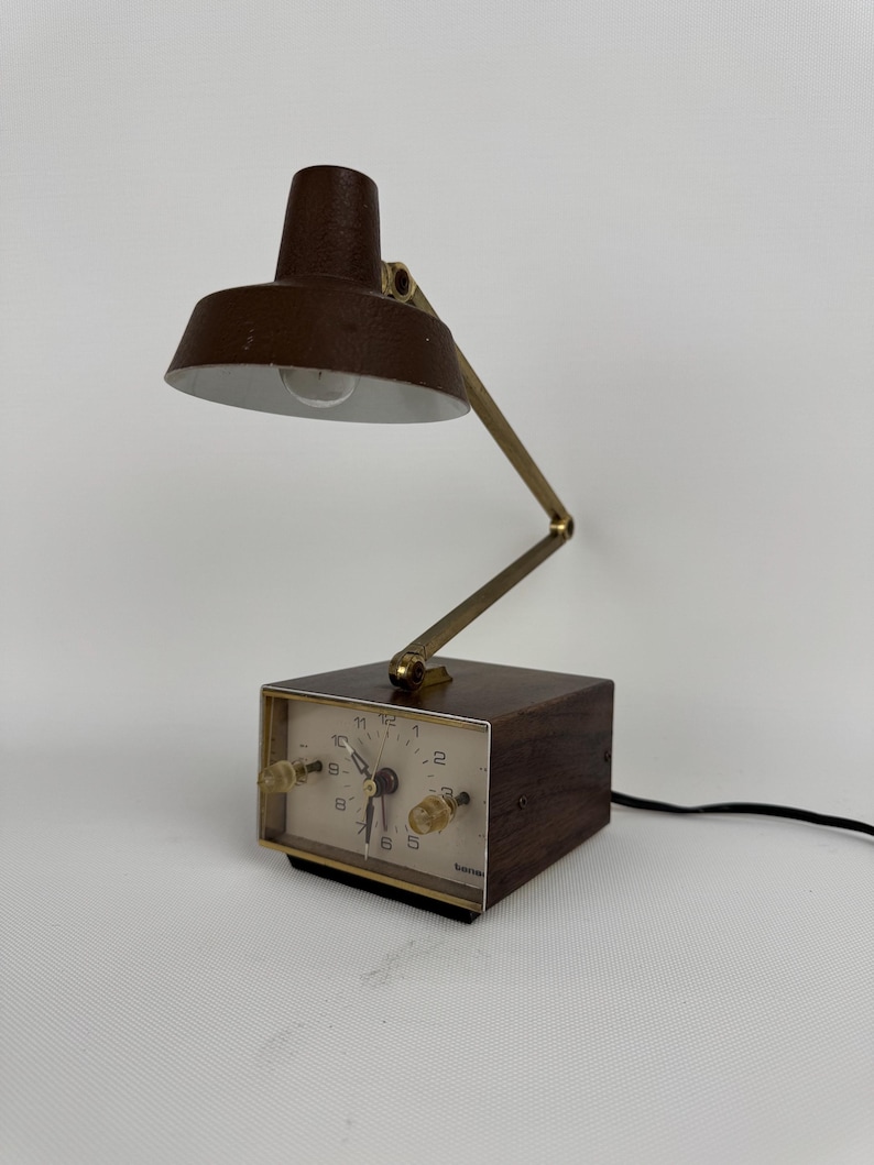 May include: A vintage brown desk lamp with a built-in clock. The lamp has a brown shade and a brass-colored adjustable arm. The clock face is white with black numerals and hands. The clock has two knobs and the word "benrus" is printed on the clock face.