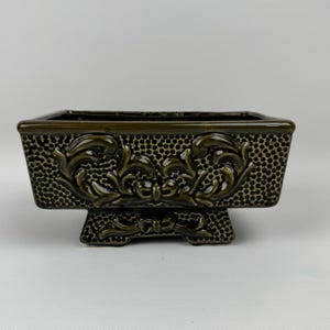 以下が含まれることがあります： 暗い緑色の長方形のセラミックプランター。装飾的な花のレリーフのディテールが施されています。 プランターは、テクスチャード加工されたドットパターンで、装飾的なベースの上にあります。 小さな植物や多肉植物に適しています。