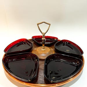 Può includere: Un vassoio da portata vintage con sei piatti triangolari. I piatti sono di un colore bordeaux intenso con un bordo rosso. Il vassoio ha una base in legno con un bordo color rame e una maniglia dorata.