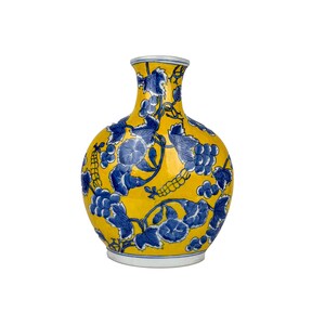 May include: A yellow ceramic vase with a blue floral design featuring grapes and leaves. The vase has a rounded body and a narrow neck. The base and rim are white.
