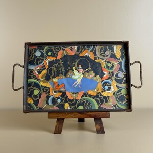 May include: A rectangular serving tray with a dark metal frame and side handles, featuring a decorative illustration of two figures in colorful costumes, a blue pond, and numerous orange and yellow butterflies against a black background.