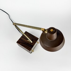 May include: A vintage brown desk lamp with a textured shade and a wooden base. The lamp features an adjustable arm with brass-colored accents and a black power cord. The base is a dark wood cube.